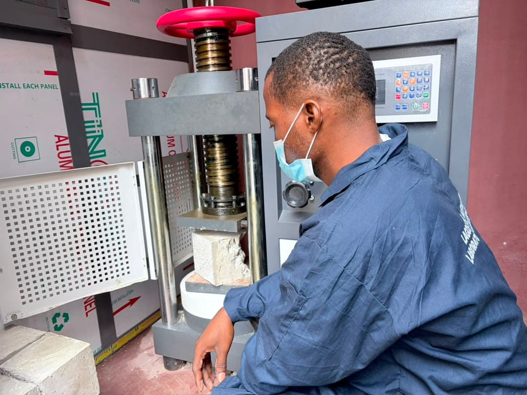 A Felmos technician at the compression testing machine, a concrete cube crushed between its platens