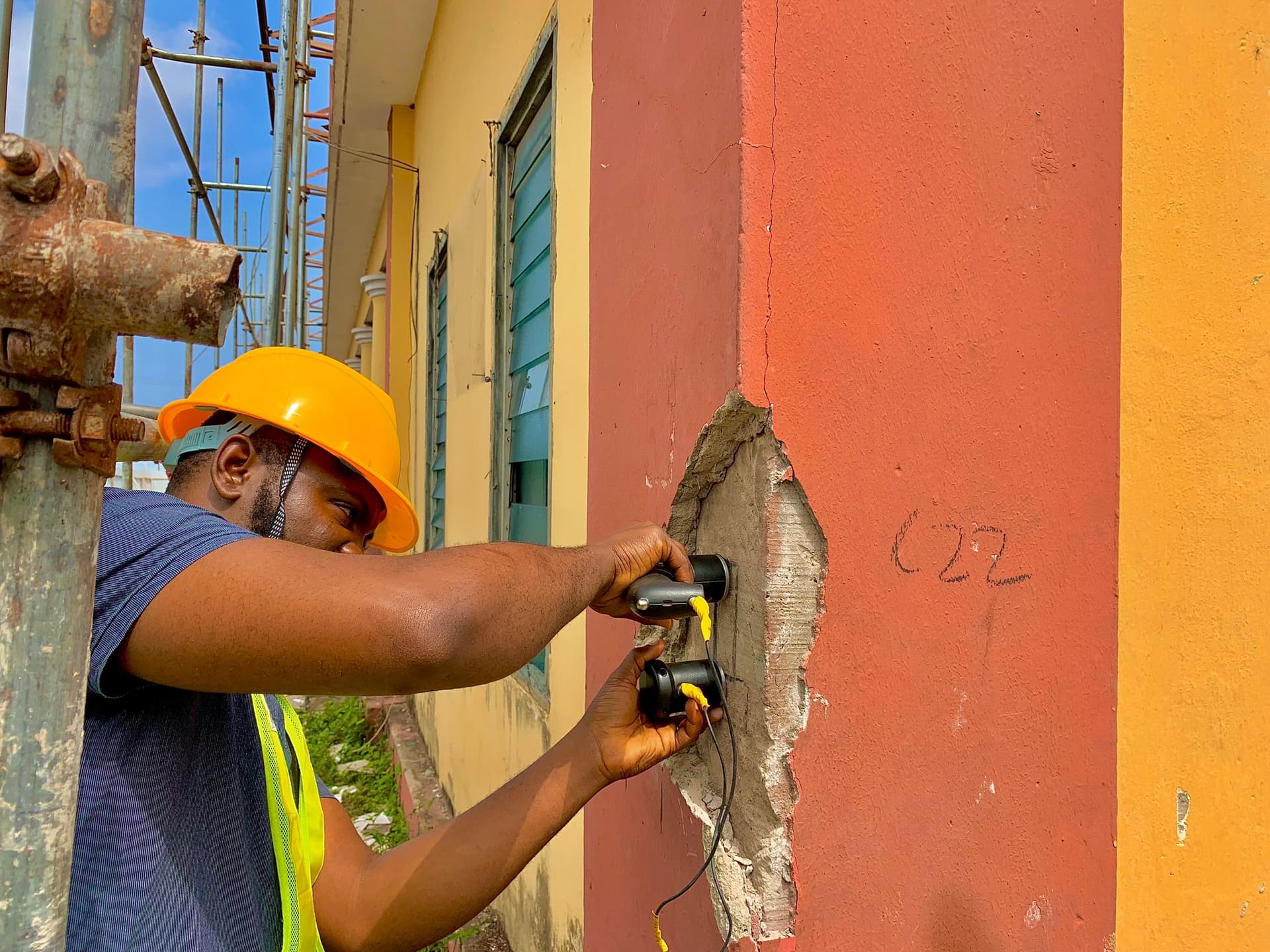A Felmos engineer holding ultrasonic pulse velocity transducers against a cracked concrete column, the render cut back to expose the concrete